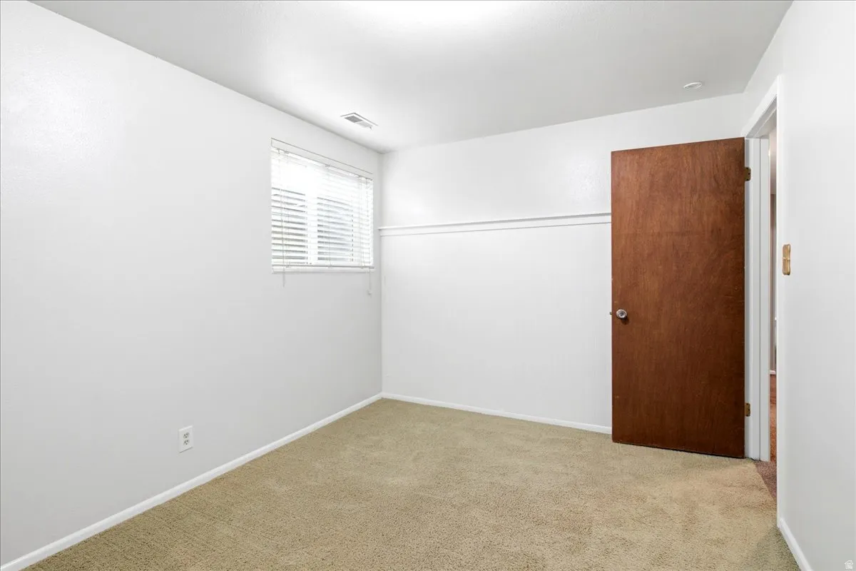 Carpeted room featuring light-colored walls, a single window with blinds, a solid wood-finish door, and recessed lighting