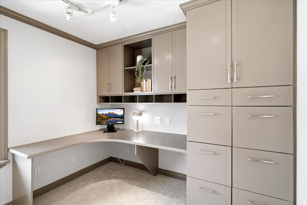 Integrated workspace featuring an L-shaped desk, built-in cabinetry, upper shelving, and track lighting