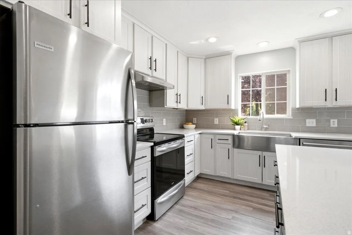 Kitchen featuring stainless steel appliances, white cabinetry, solid surface countertops, a farmhouse sink, and wood-finish flooring