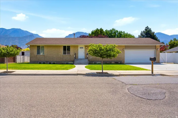 Brick ranch-style home featuring a two-car garage, concrete driveway, and mature landscaping