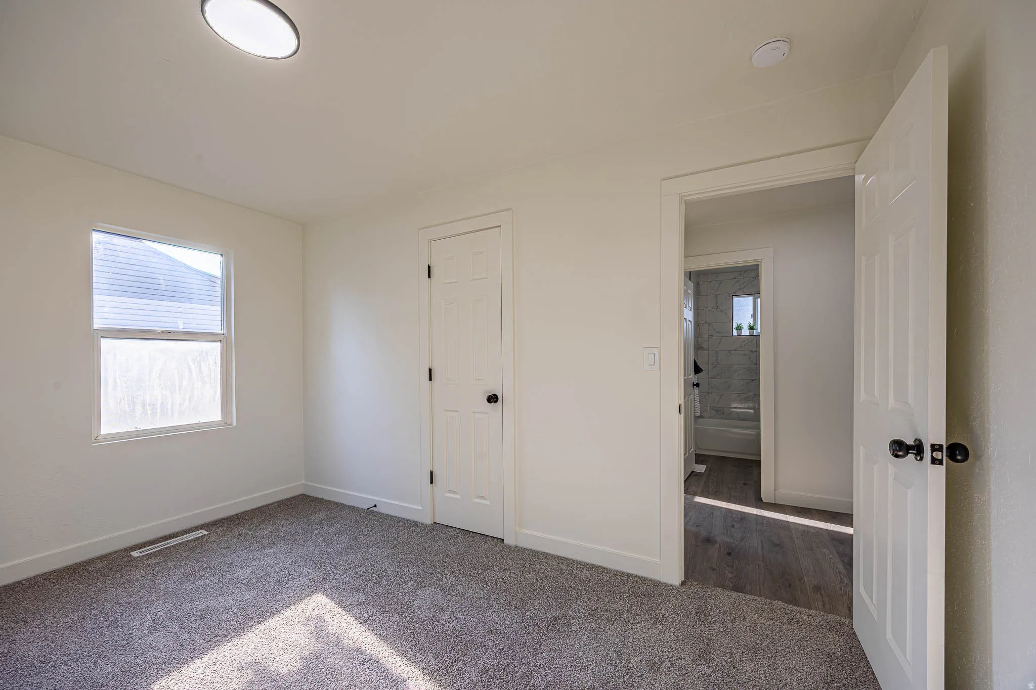 Carpeted room featuring a single window with blinds, a white paneled door, and a flush-mount ceiling light