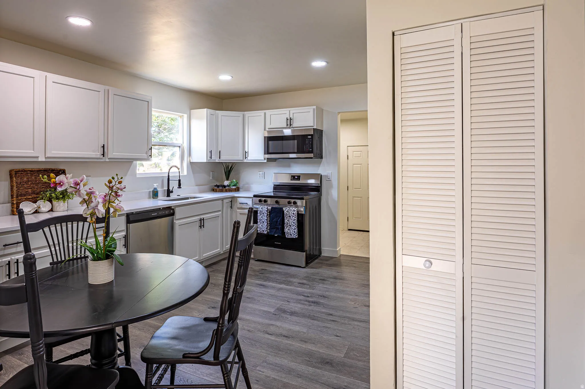 Kitchen featuring white cabinetry, stainless steel appliances, wood-finish flooring, recessed lighting, and a window with natural light