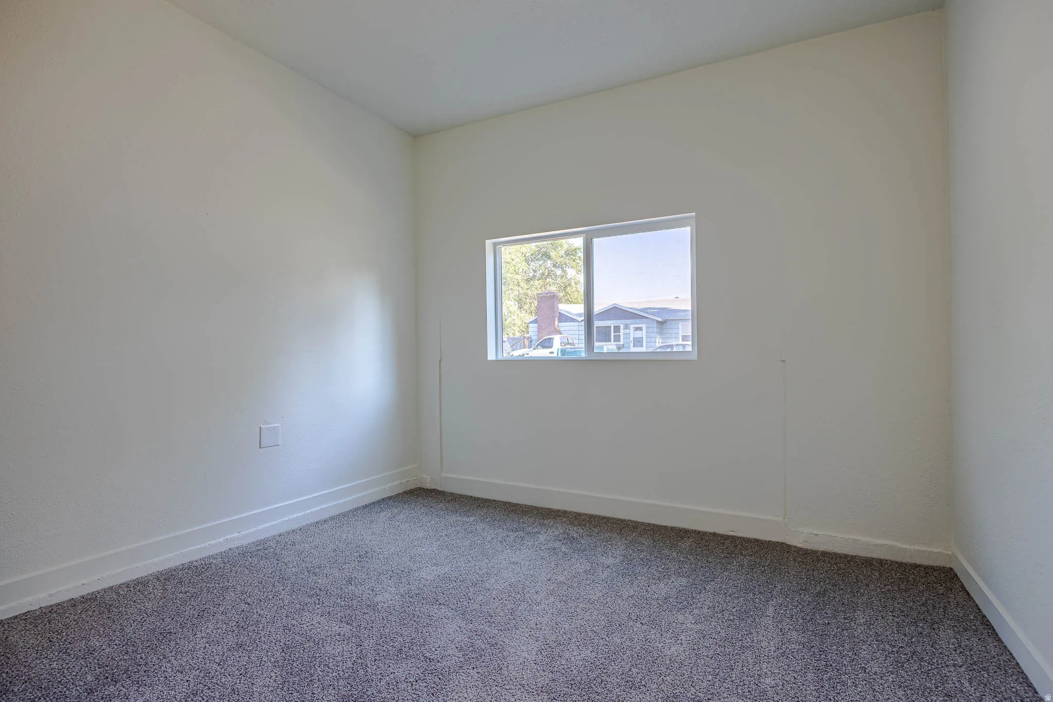 Light-filled interior space featuring neutral wall tones, white baseboards, and gray textured carpeting