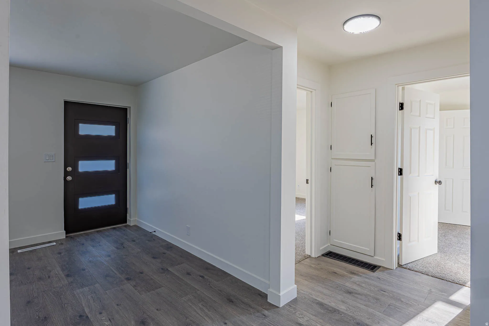 Entryway featuring wood-finish flooring, a contemporary front door with horizontal glass inserts, white baseboards, and a built-in white cabinet with black hardware