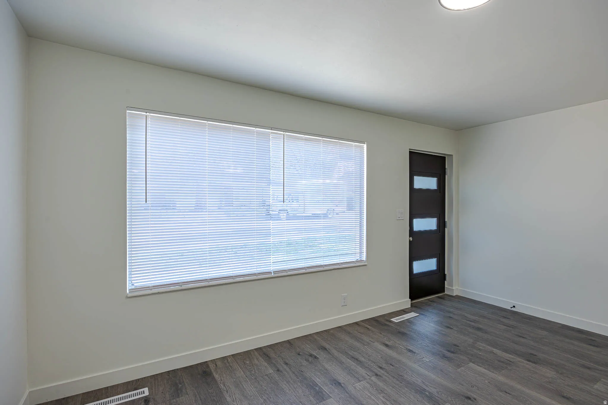 Spacious room featuring wood-finish flooring, white baseboards, and a modern entry door with frosted glass panels