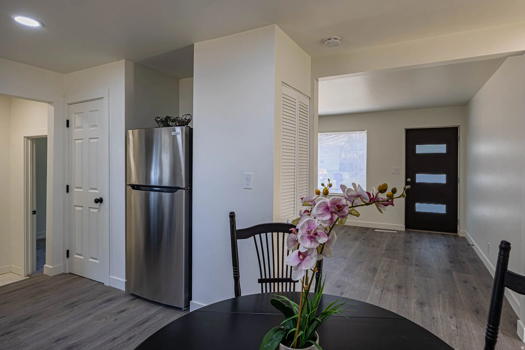 Open concept living area featuring dark wood-finish flooring, a contemporary dark entry door with horizontal glass panels, and a prominent stainless steel refrigerator