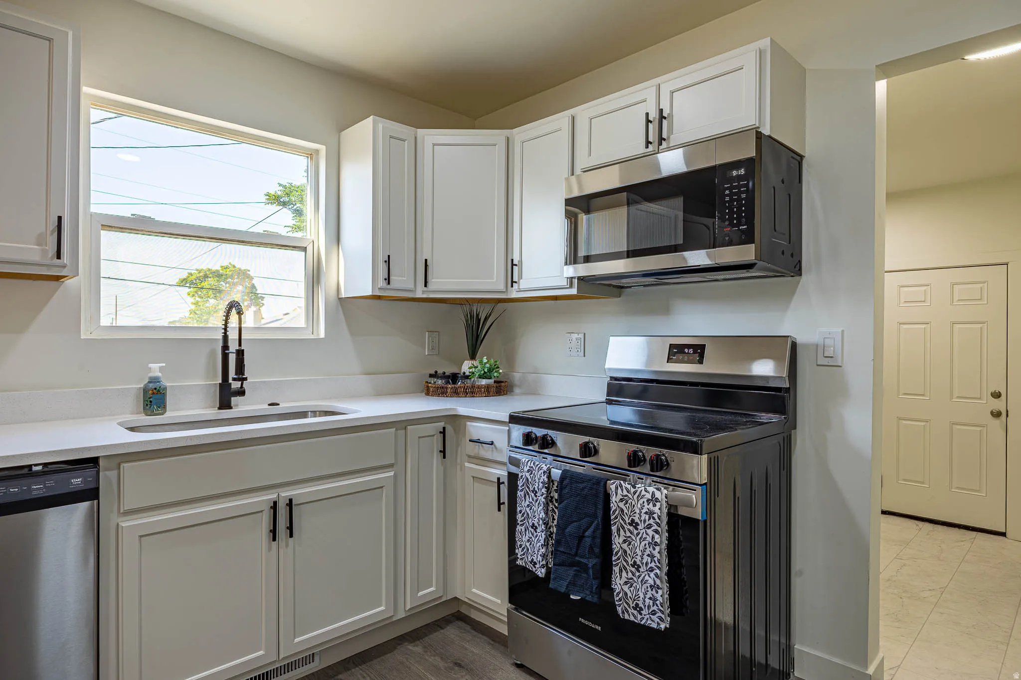 Contemporary kitchen featuring white cabinetry with black hardware, stainless steel appliances, a window above the sink, and light-toned countertops