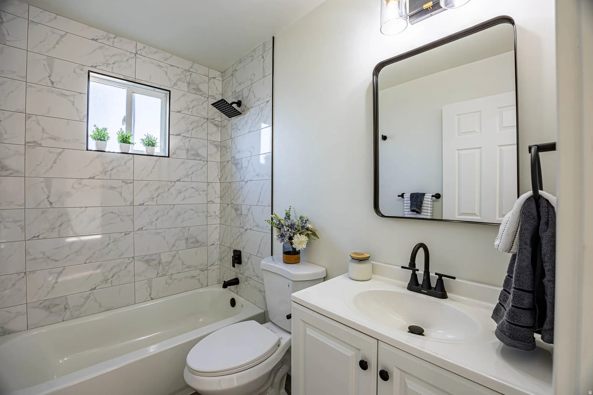 Full bathroom featuring a white vanity with integrated sink, matte black fixtures, a rectangular framed mirror, and a tiled shower-tub combination with a rain showerhead