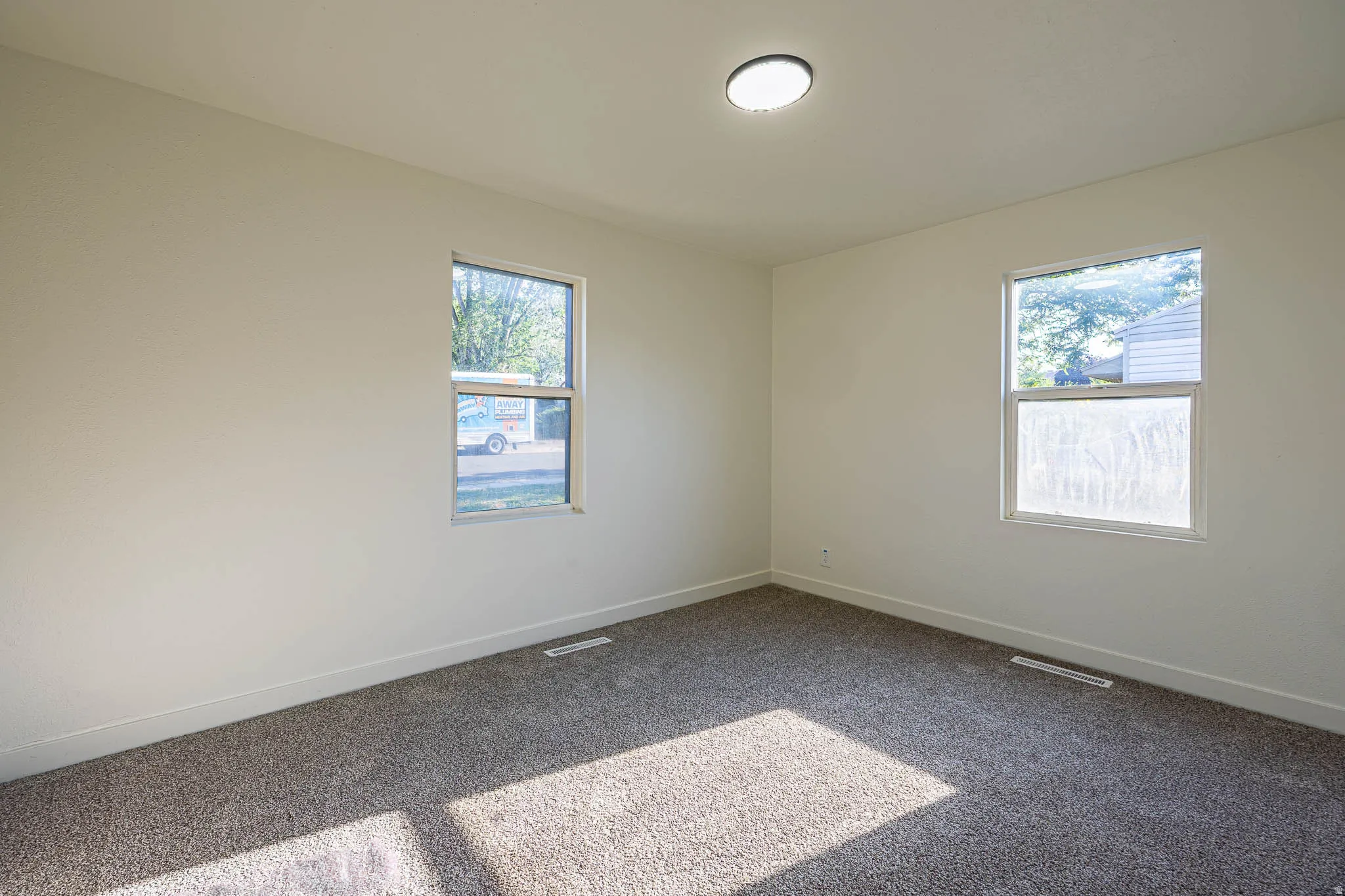 Carpeted room with two windows and a flush-mount ceiling light fixture