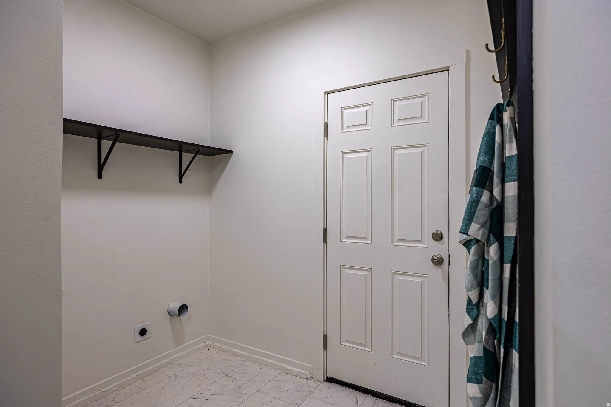 Dedicated utility space featuring a five-panel entry door with brushed nickel hardware, light-toned tile flooring, and a built-in wall shelf with black metal brackets