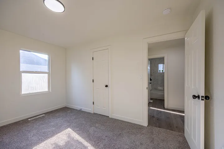 Carpeted room featuring a single window with blinds, a white paneled door, and a flush-mount ceiling light