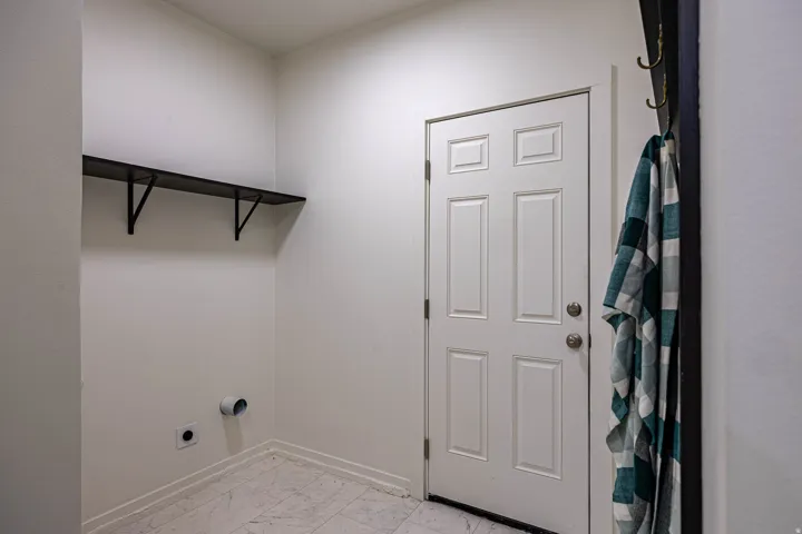 Dedicated utility space featuring a five-panel entry door with brushed nickel hardware, light-toned tile flooring, and a built-in wall shelf with black metal brackets