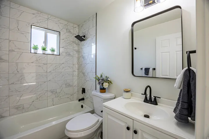 Full bathroom featuring a white vanity with integrated sink, matte black fixtures, a rectangular framed mirror, and a tiled shower-tub combination with a rain showerhead