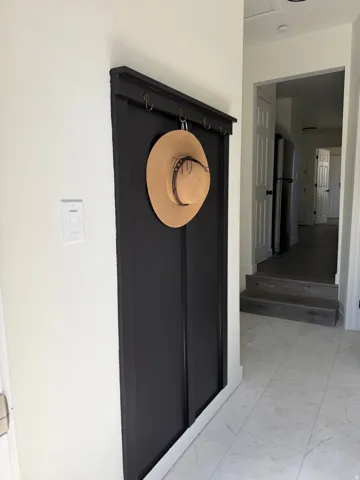 Entryway featuring light-toned tile flooring and a built-in black coat rack with brass-toned hooks