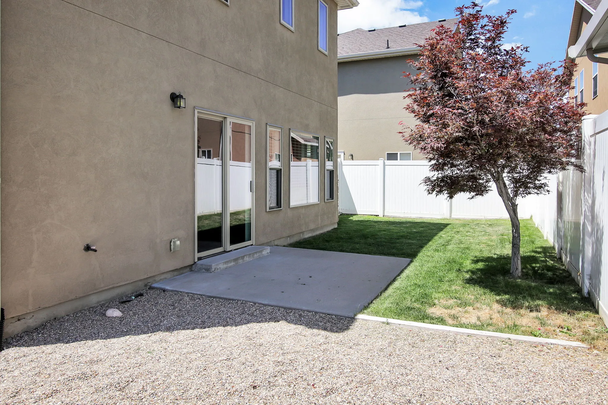 Private backyard featuring a concrete patio, green lawn, mature tree, and white vinyl fencing