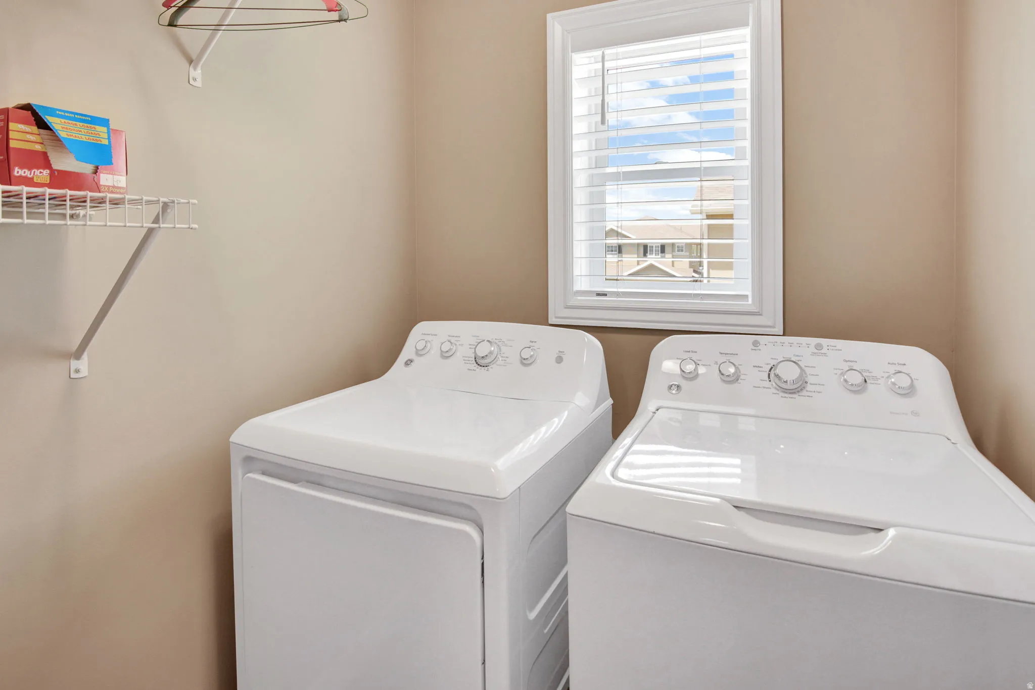 Dedicated laundry space featuring a window with white blinds, white wire shelving, and neutral wall paint