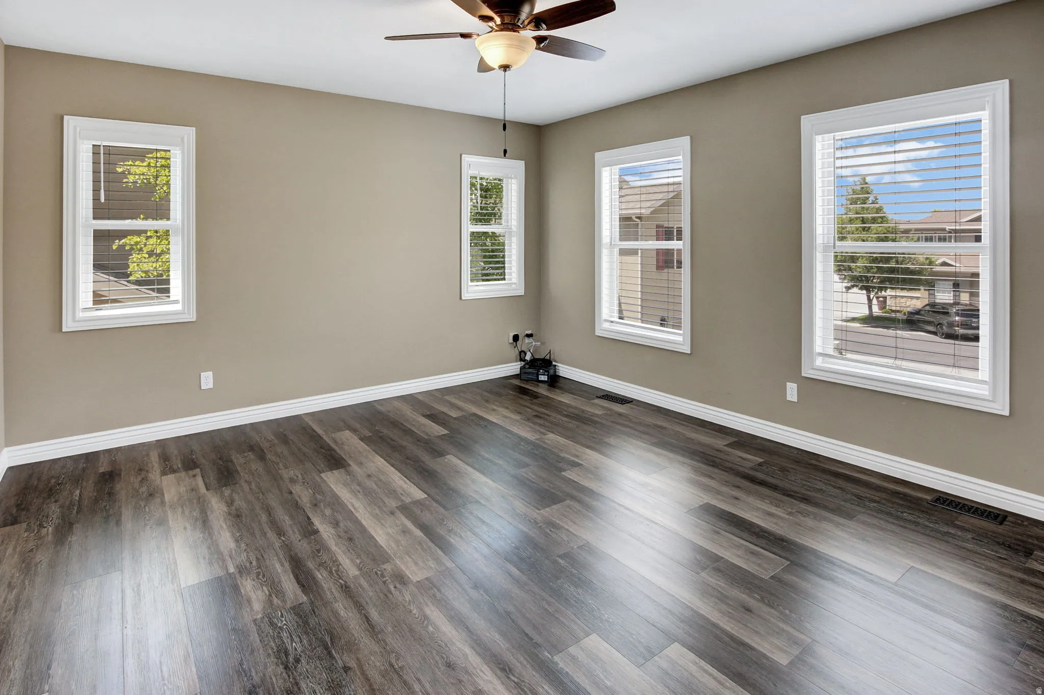 Spacious room featuring wood-finish flooring, light tan walls, and multiple windows with white blinds