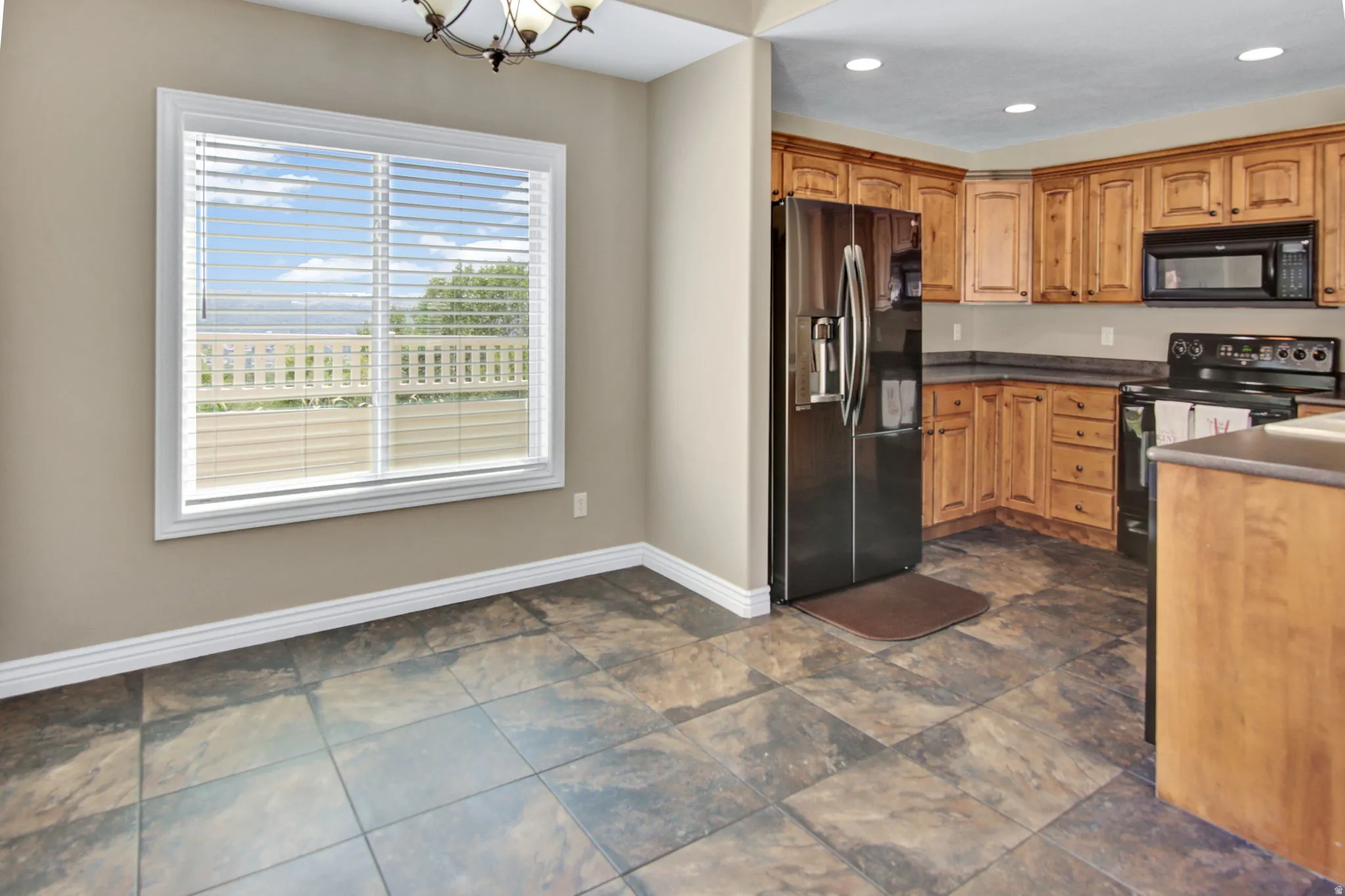 Kitchen and dining area featuring light wood cabinetry, dark countertops, and black appliances
