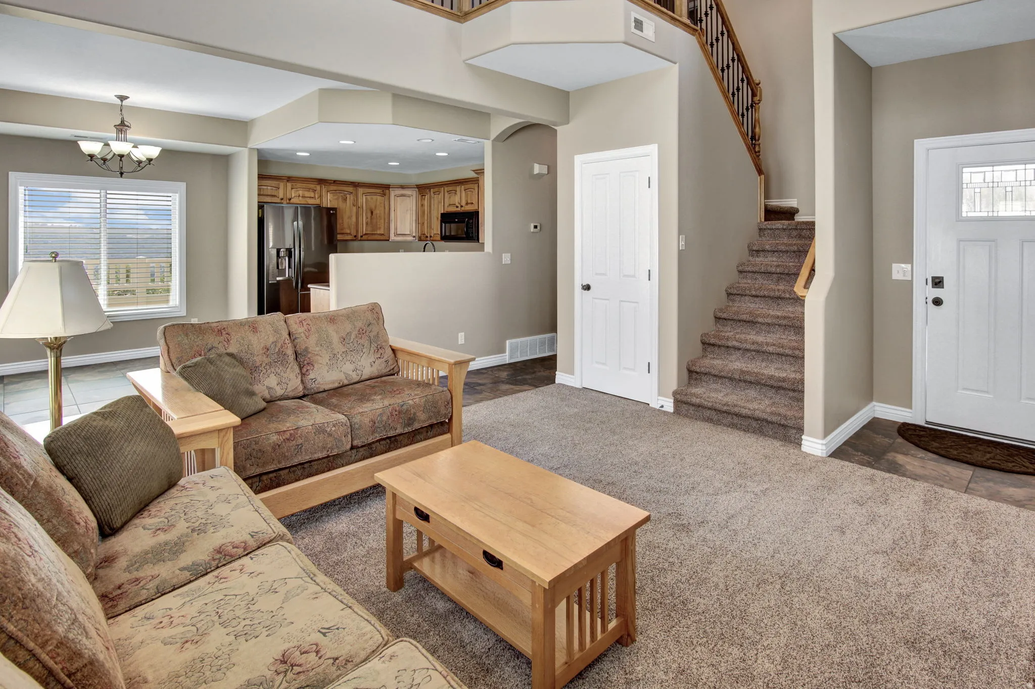 Open-concept living area featuring a neutral color palette, carpeted flooring, and a staircase with a wood banister