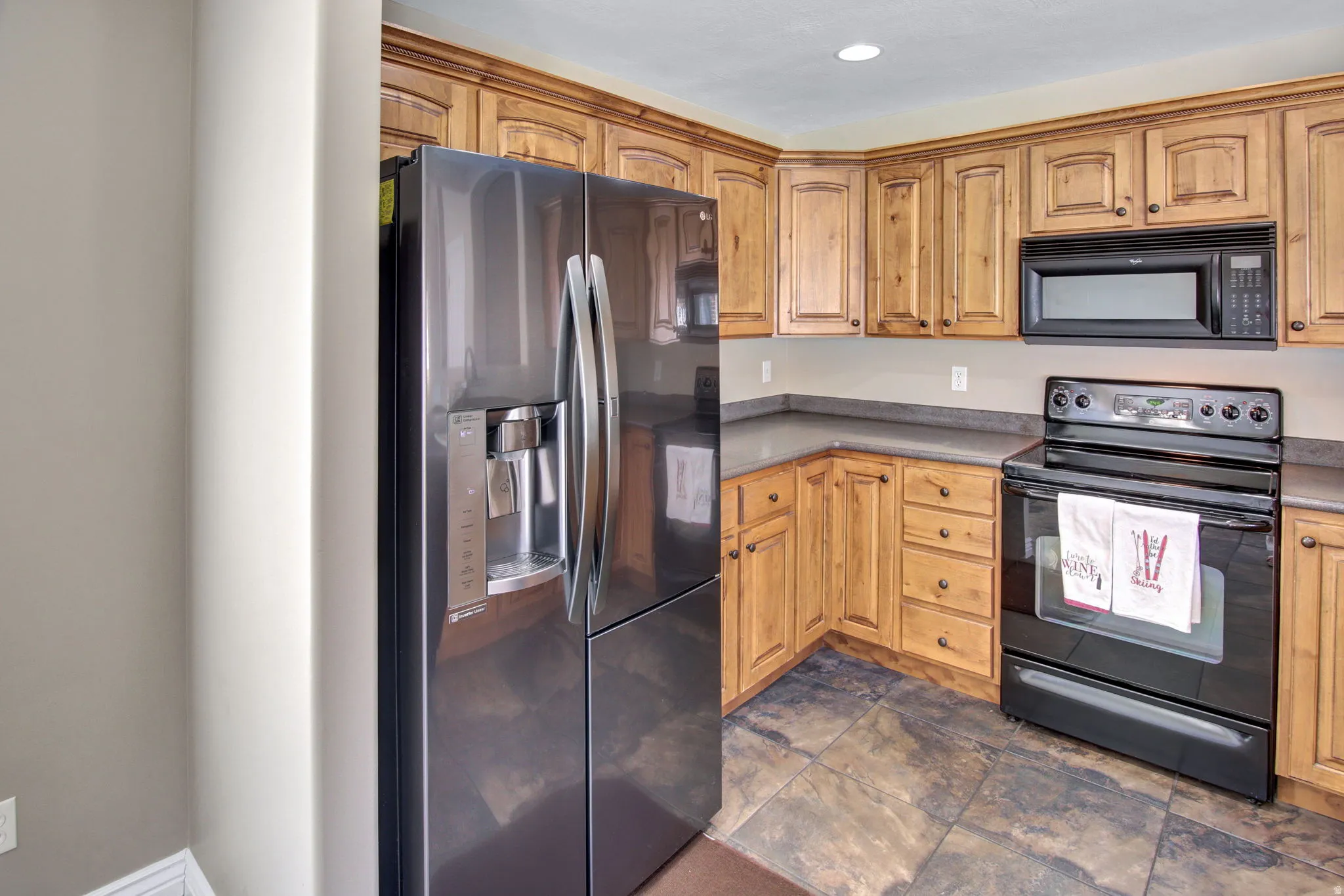 Kitchen featuring wood cabinetry, dark countertops, a built-in microwave, an electric range, and a side-by-side refrigerator