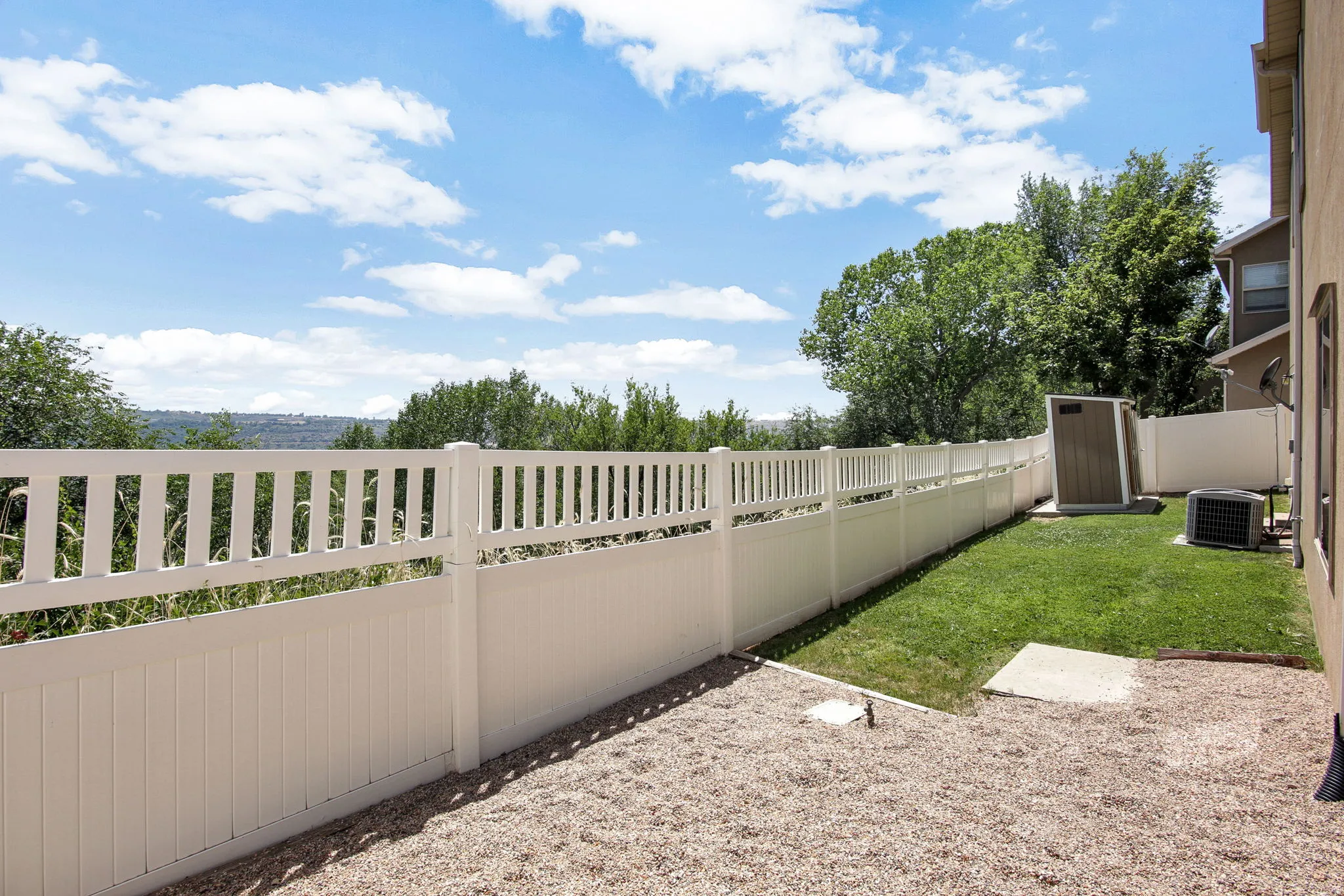 Expansive outdoor space featuring a white privacy fence, green lawn, and a gravel area