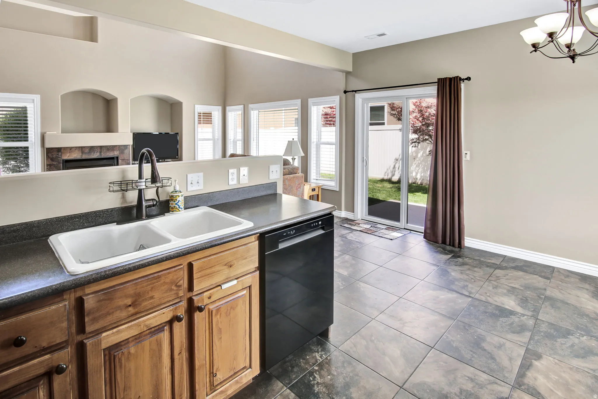 Kitchen featuring wood cabinetry, a double basin sink with a gooseneck faucet, a built-in dishwasher, and a dark countertop