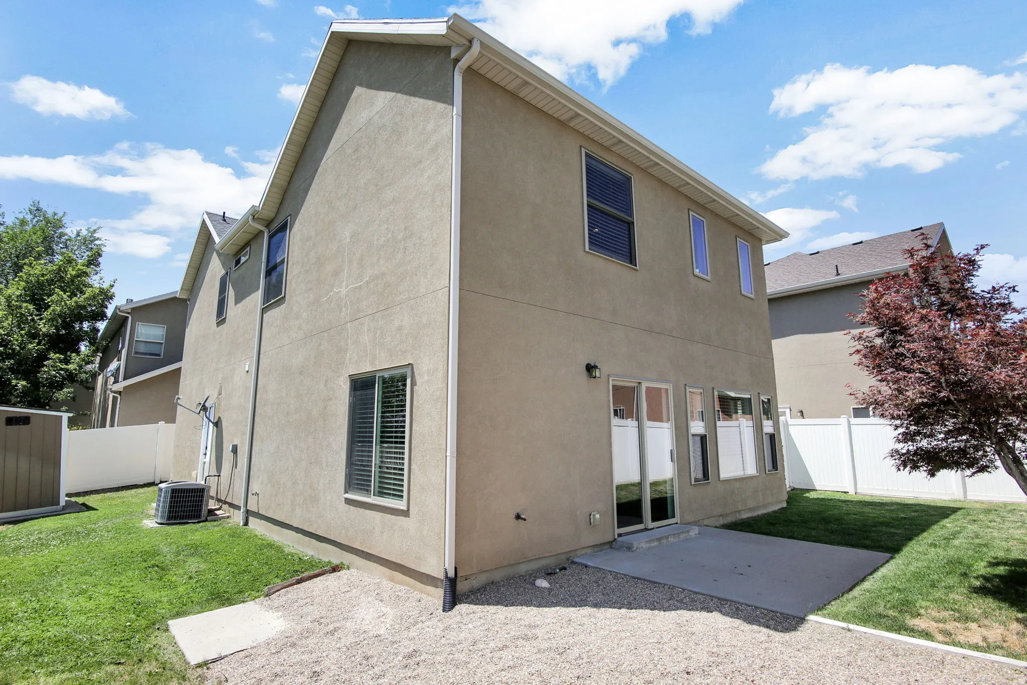 Rear exterior featuring a concrete patio, green lawn, white privacy fencing, and an exterior shed