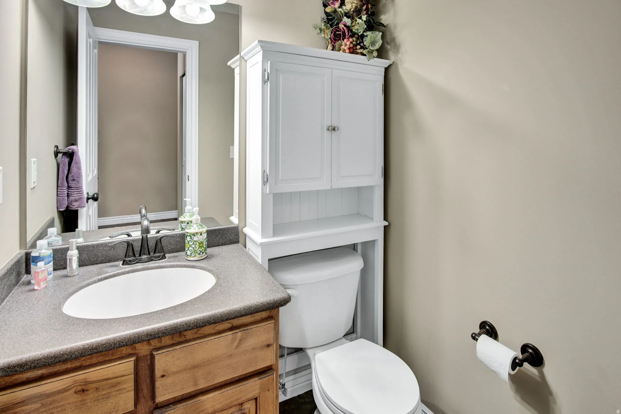 Bathroom featuring a wood-finish vanity with an integrated sink and dark countertop