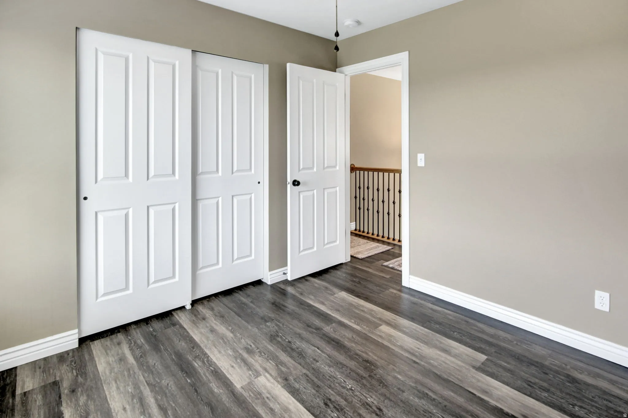 Spacious room featuring wood-finish flooring, light tan walls, white baseboards, and white paneled doors