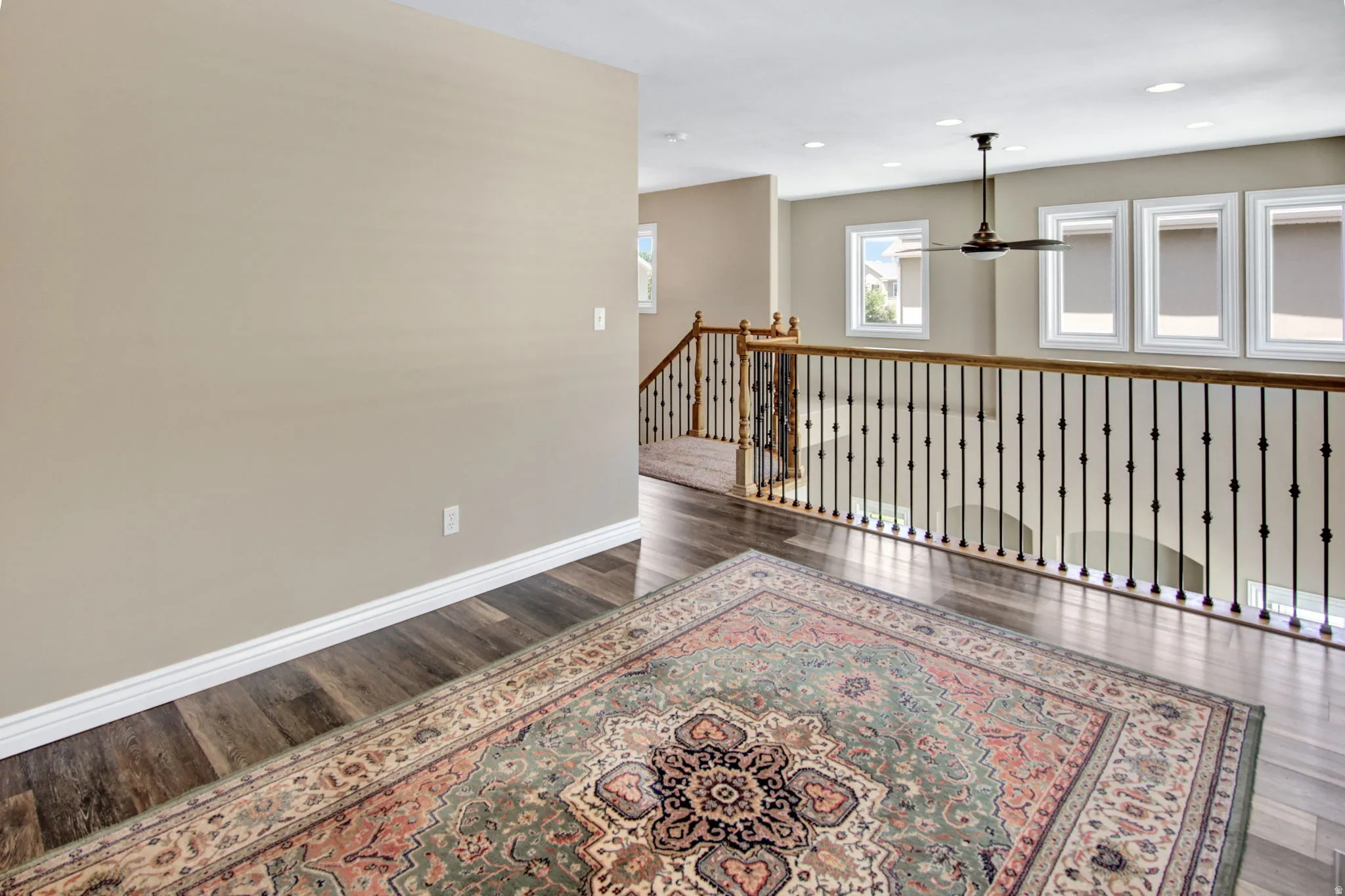 Upper-level landing featuring wood-finish flooring, a decorative railing with wooden top rail and black balusters, and multiple windows