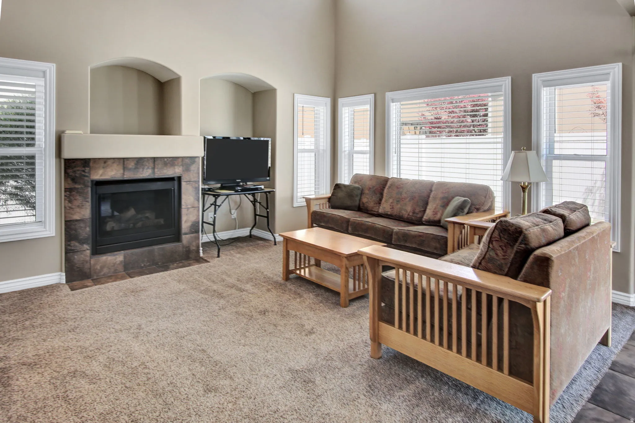Living area featuring a tiled fireplace with a mantel, two arched wall niches, multiple windows with blinds, and carpeted flooring