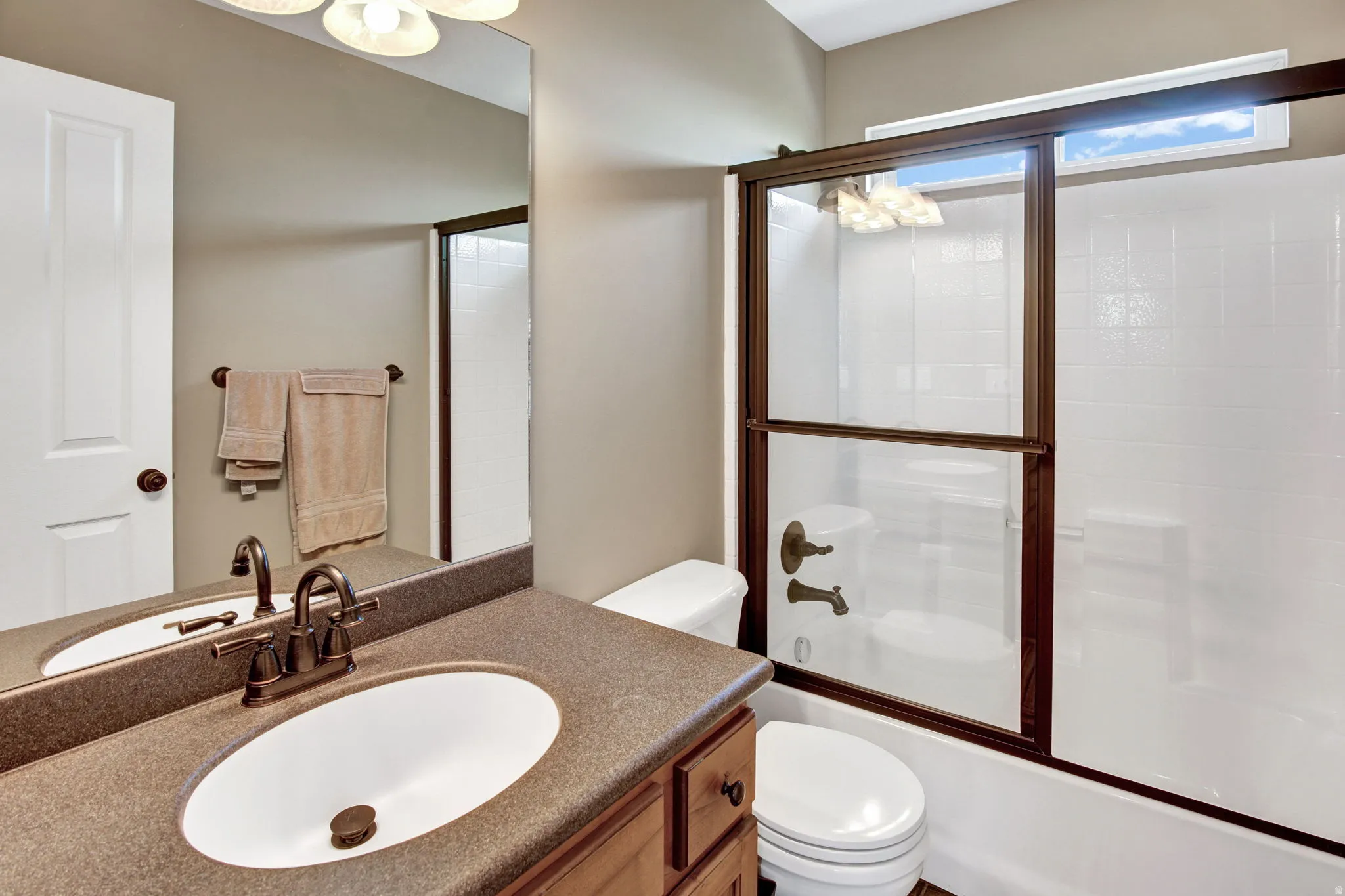 Full bathroom featuring a wood-finish vanity with a single basin sink and dark countertop, bronze-toned faucet, mirror, toilet, and a combination tub and shower with sliding glass doors