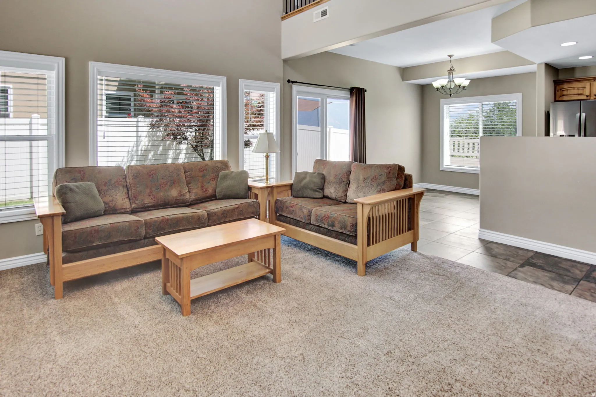 Spacious living area featuring neutral-toned walls, high ceilings, and a combination of carpet and tile flooring