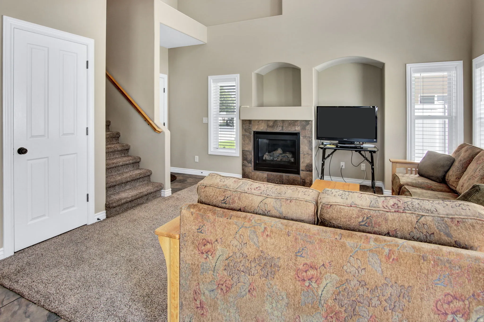 Living area featuring a tiled fireplace with mantel, built-in wall niches, and multiple windows with blinds