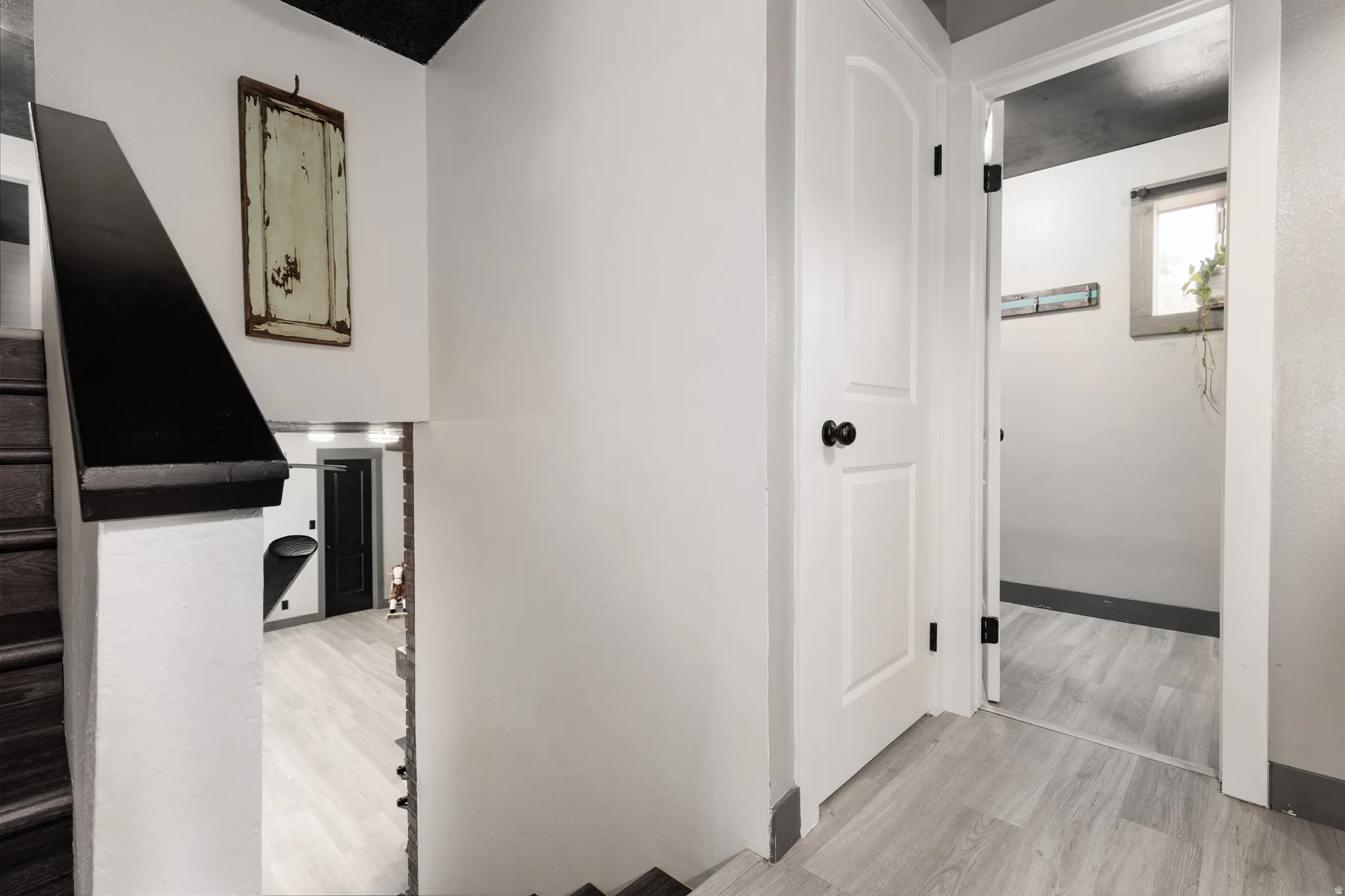 Staircase with dark wood treads and a black handrail leading to a lower level featuring light wood-finish flooring