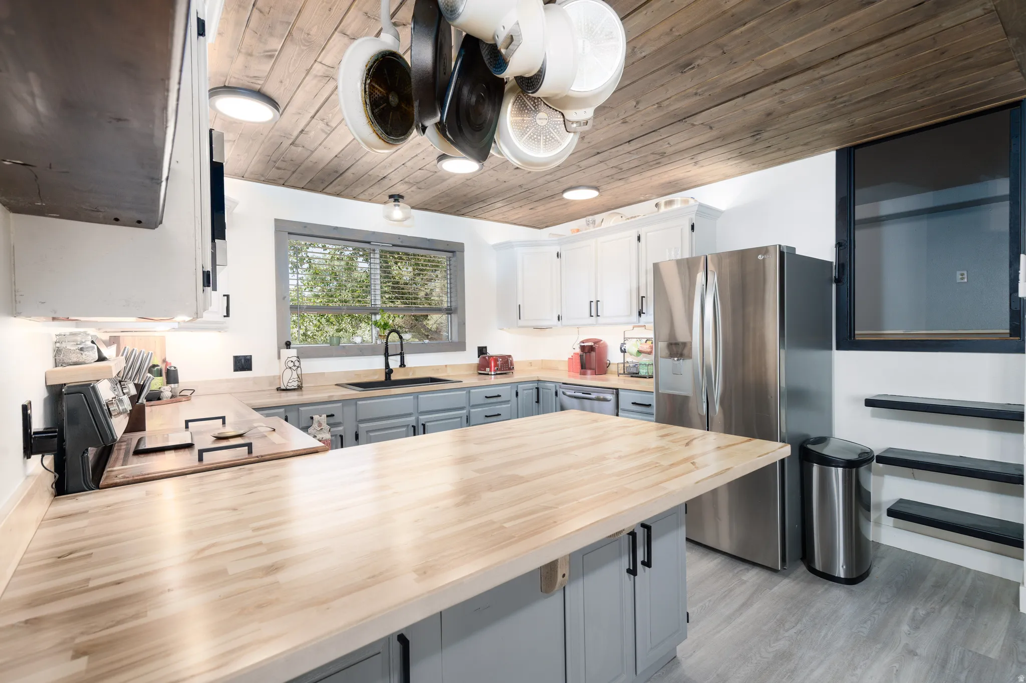 Kitchen featuring extensive wood-finish countertops, two-tone cabinetry with black hardware, stainless steel refrigerator, and wood plank ceiling