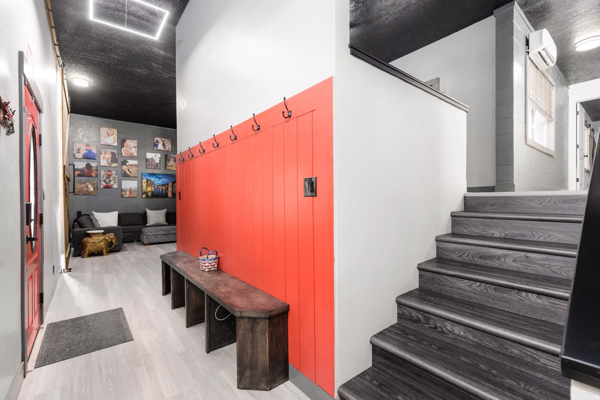 Entryway featuring light-toned wood-finish flooring, a vibrant red accent wall with integrated coat hooks, and a dark wood-finish staircase