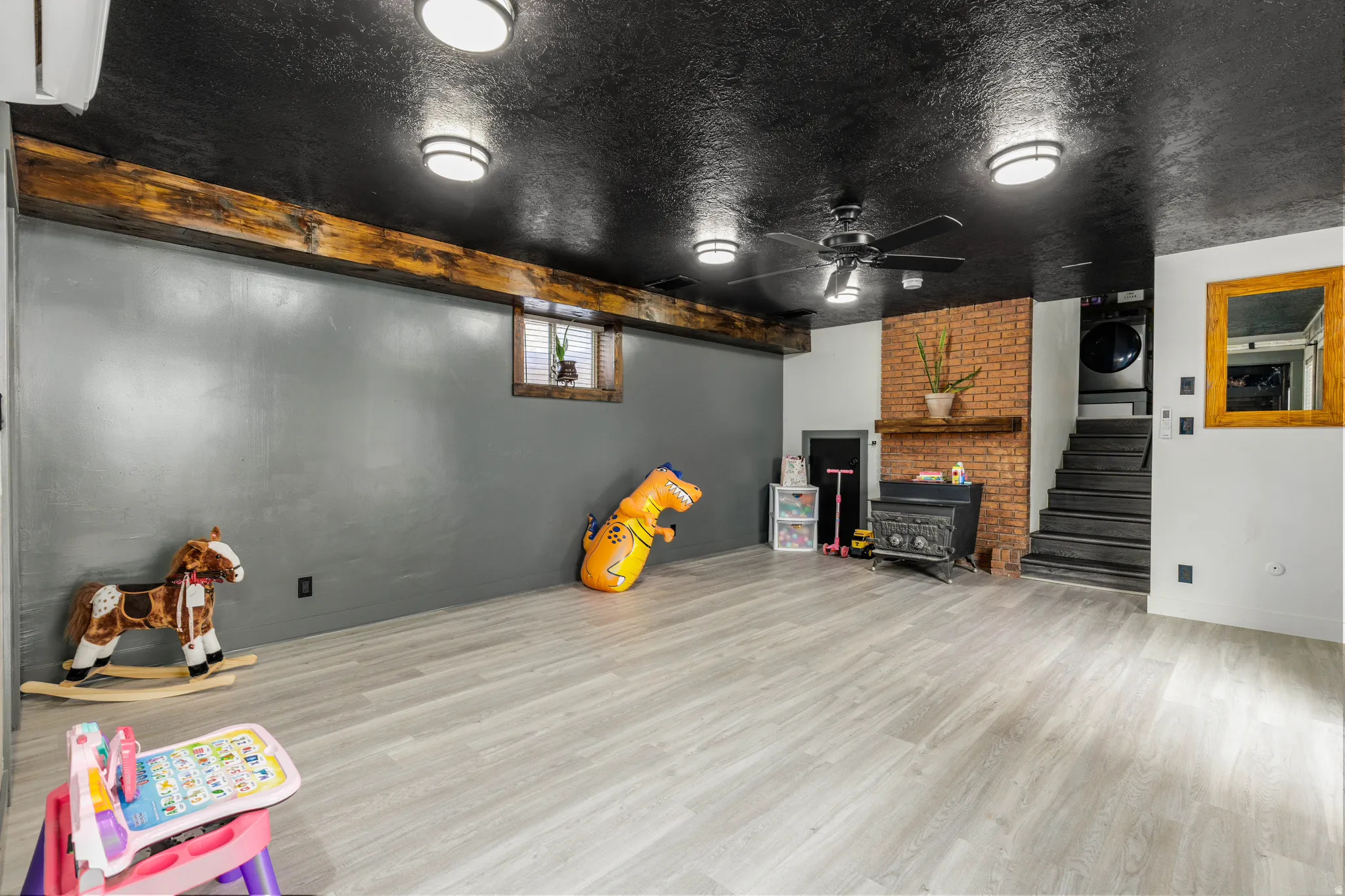 Spacious lower level featuring light wood-finish flooring, a wood-burning stove with a brick surround and wood mantel, a ceiling fan, and recessed lighting