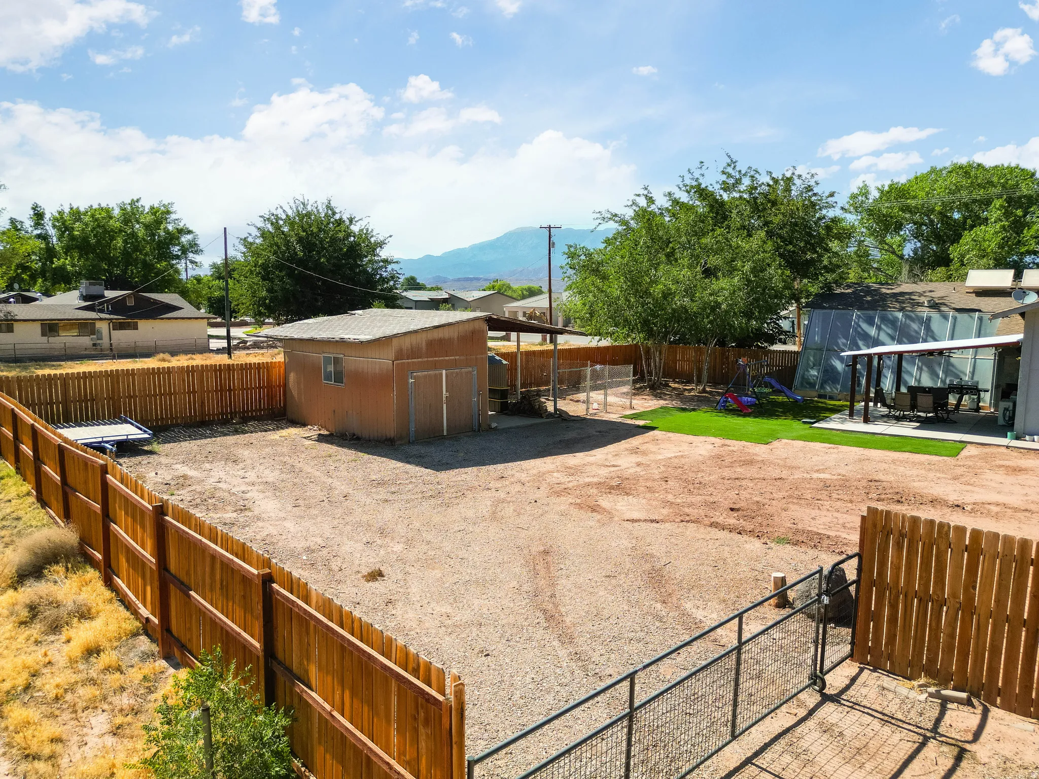 Expansive fenced backyard featuring a storage shed, gravel ground cover, and a dedicated artificial turf area with an attached patio cover