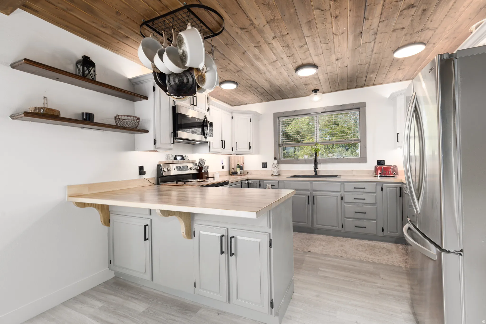 Kitchen featuring a wood-finish plank ceiling, light wood-finish countertops, grey lower cabinetry, white upper cabinetry, and stainless steel appliances