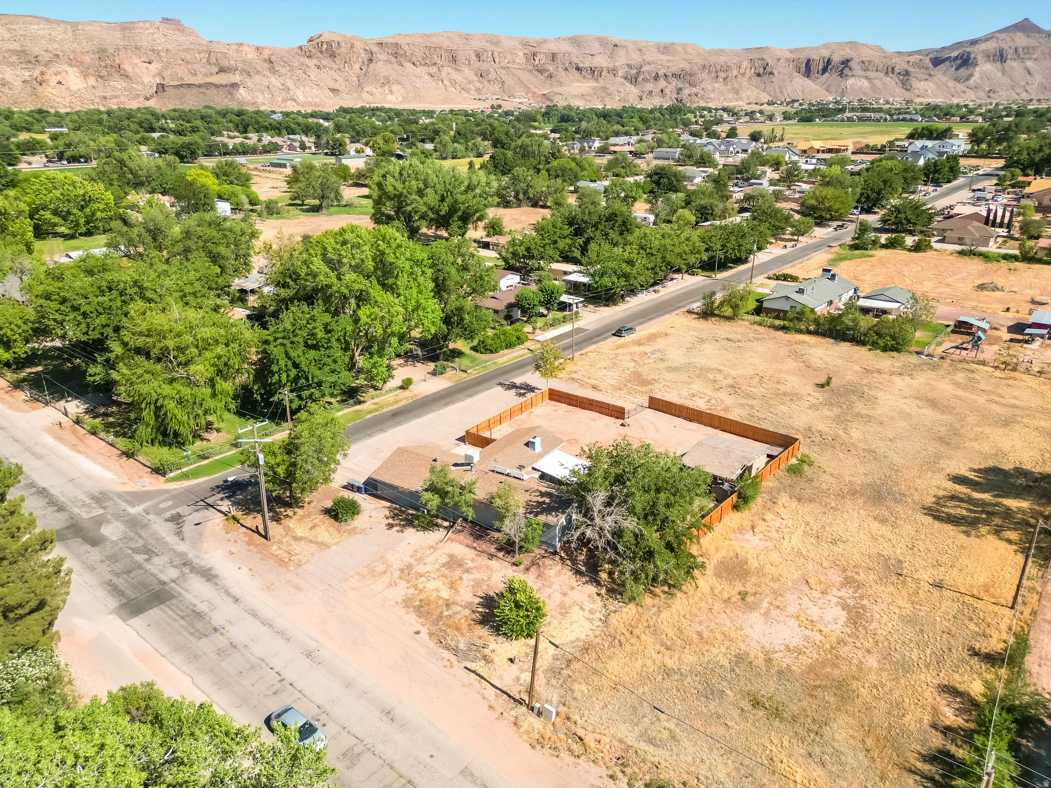 Expansive property featuring a single-story residence with a brown shingle roof, a privacy fence, and mature trees