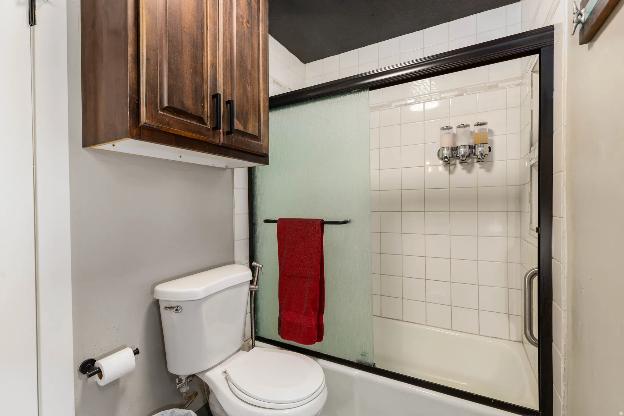 Bathroom featuring a white toilet, dark wood cabinetry, and a shower with a sliding glass door