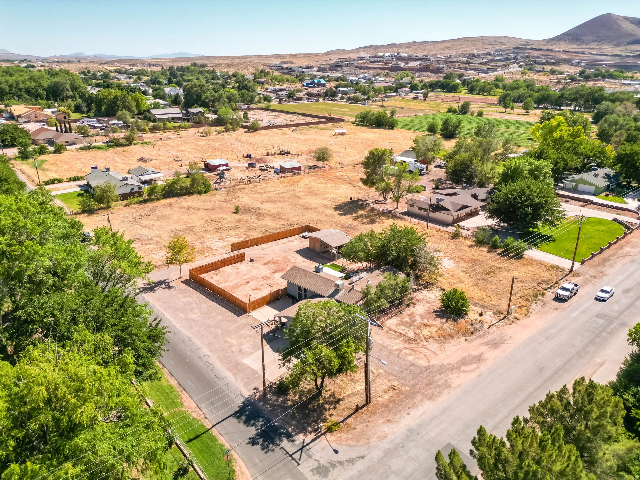 Expansive property featuring a single-story residence with a brown roof, surrounded by mature trees and open land