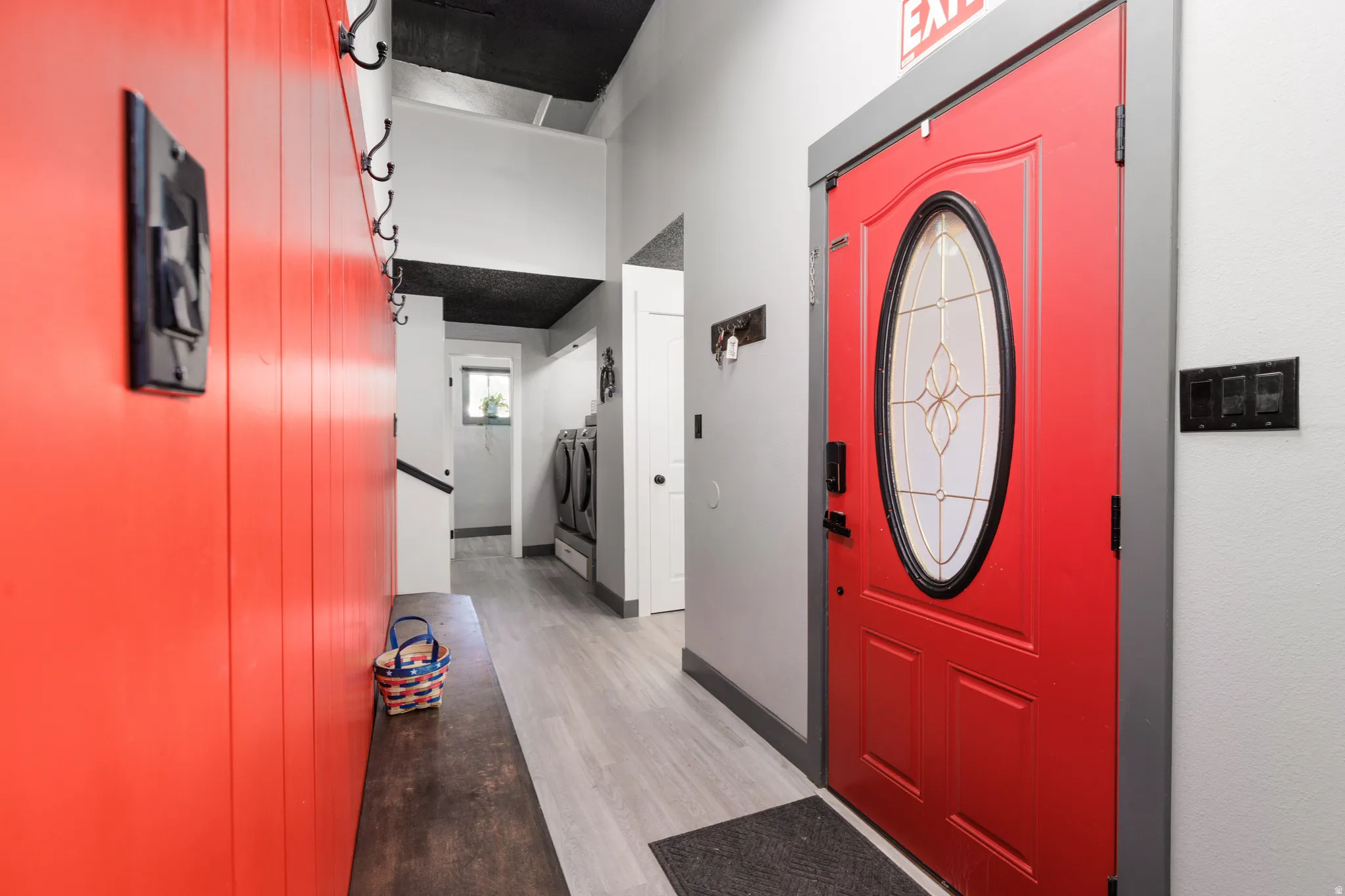 Entryway featuring a vibrant red oval-light door, light wood-finish flooring, and a contrasting black ceiling