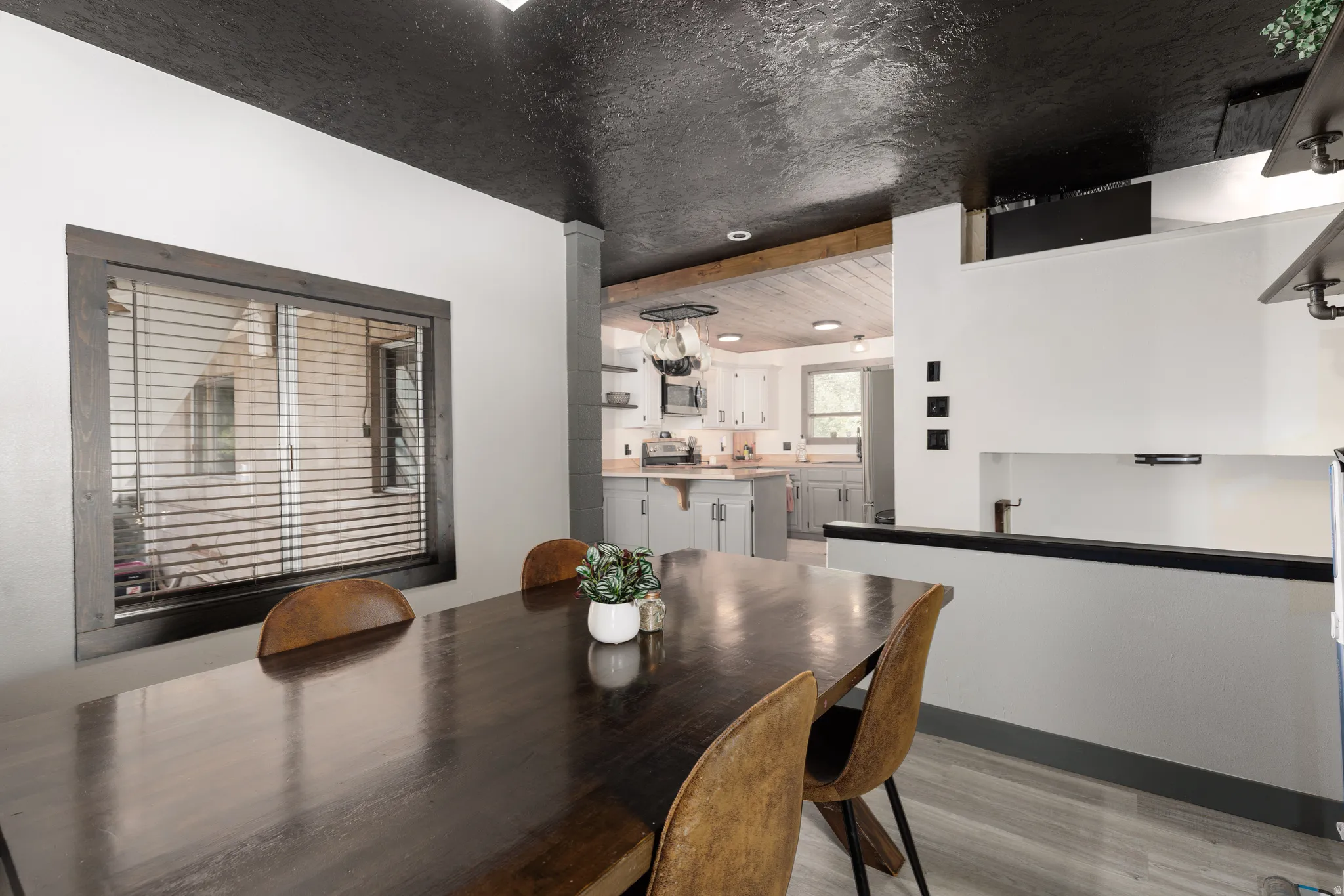 Dining area featuring a dark wood-finish table, plank-style flooring, a dark-stained window frame, and a contrasting dark ceiling