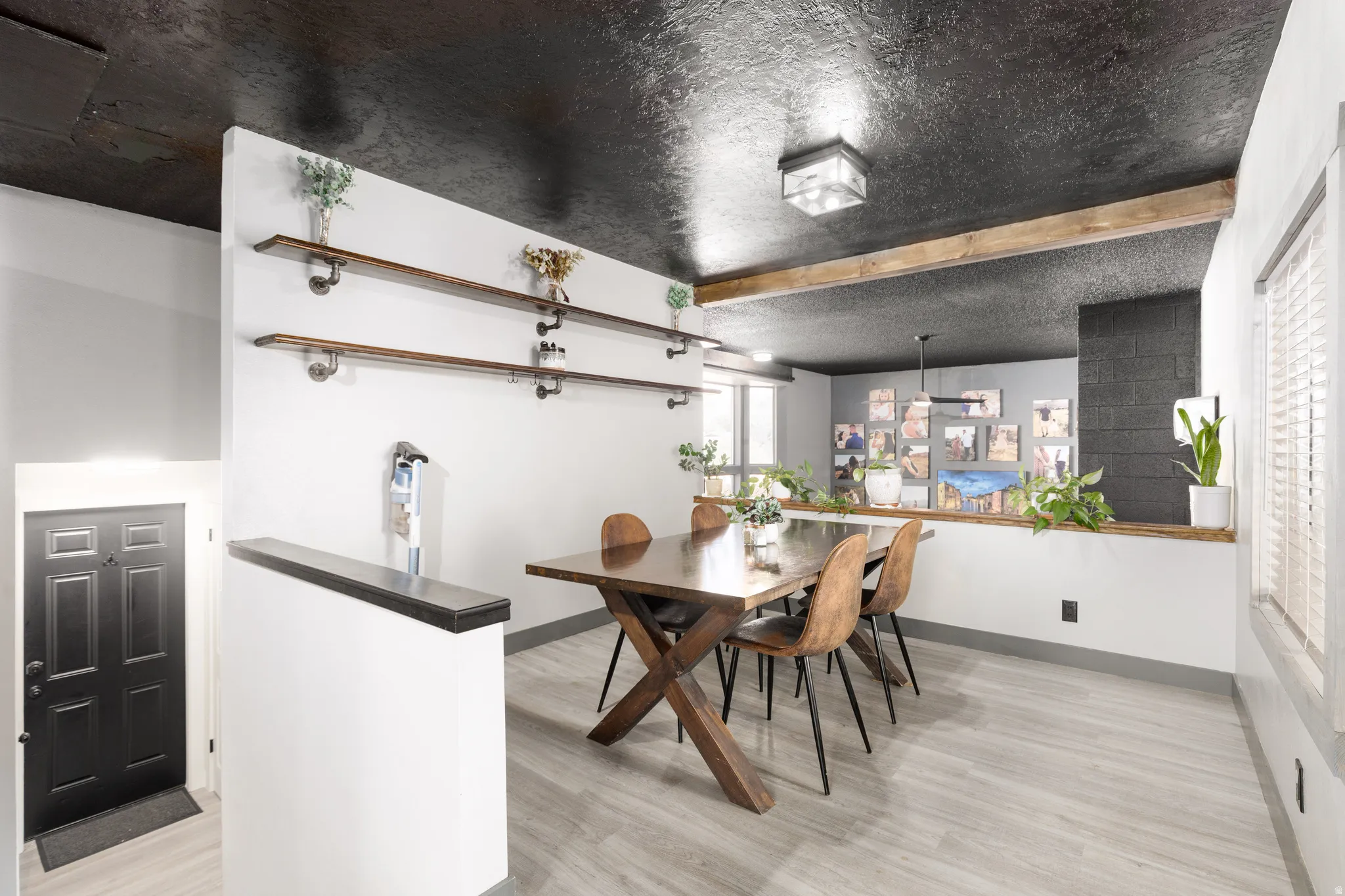Dining area featuring light wood-finish flooring, a dark textured ceiling, and a prominent wood beam