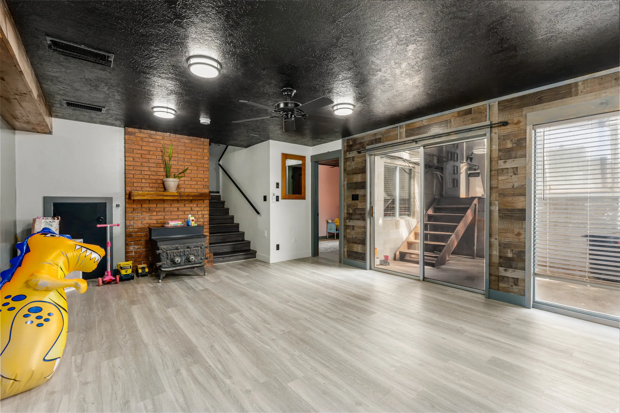 Spacious room featuring light wood-finish flooring and a textured black ceiling with recessed lighting and a ceiling fan
