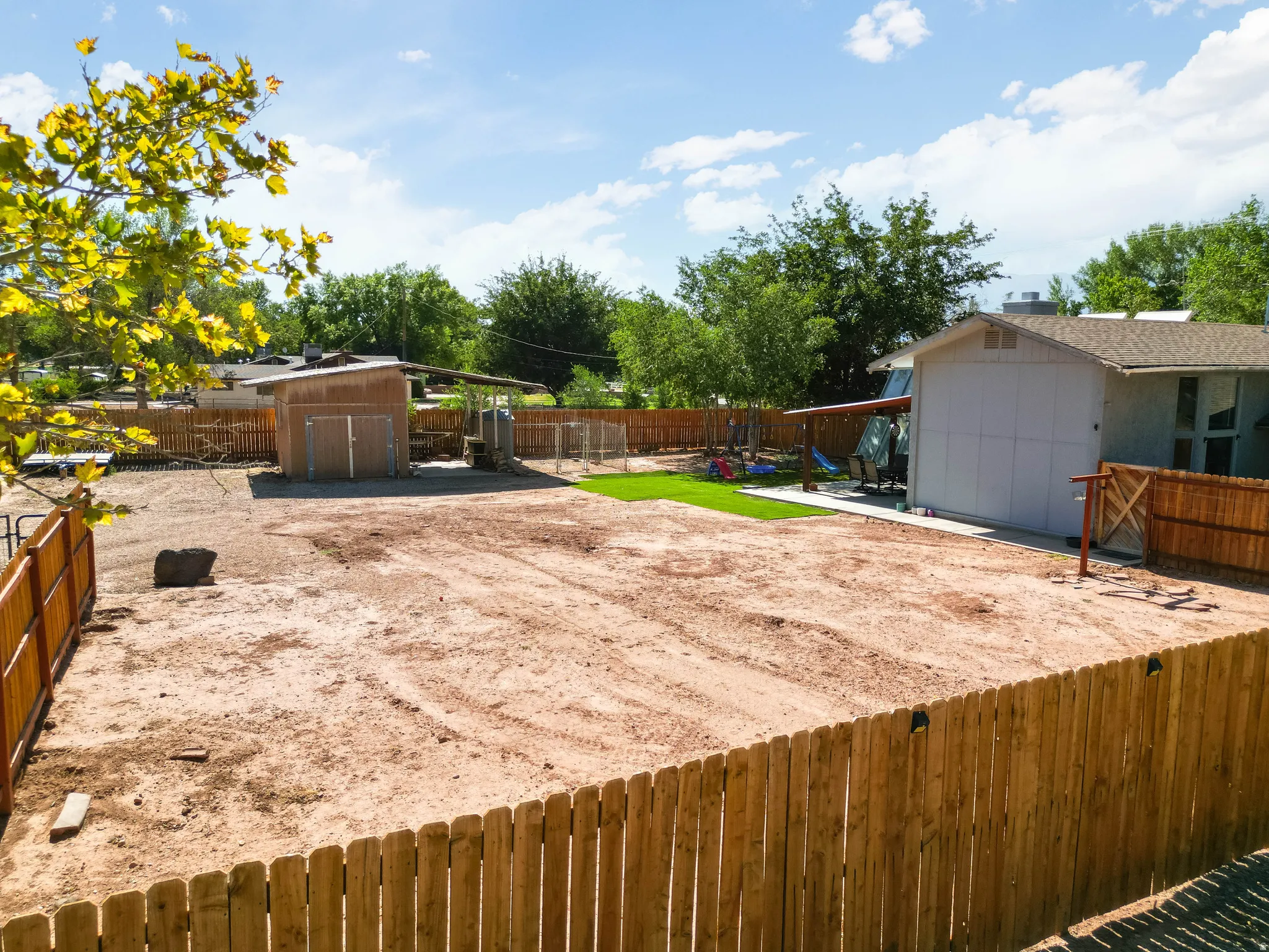 Expansive fenced backyard featuring a large cleared area, a separate storage shed, a covered patio, and a small artificial turf section