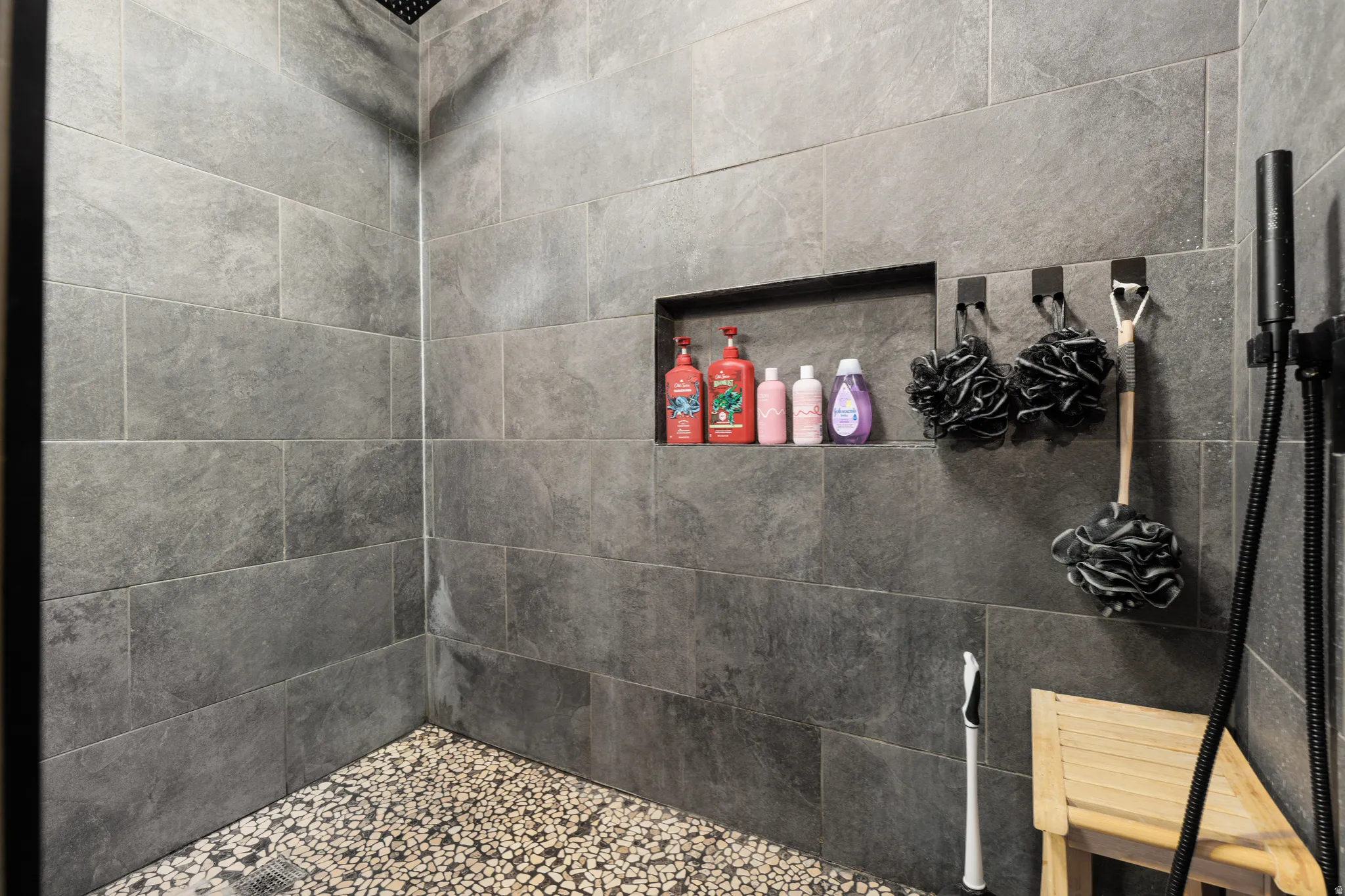 Walk-in shower featuring large format grey tile walls and a contrasting pebble-stone floor