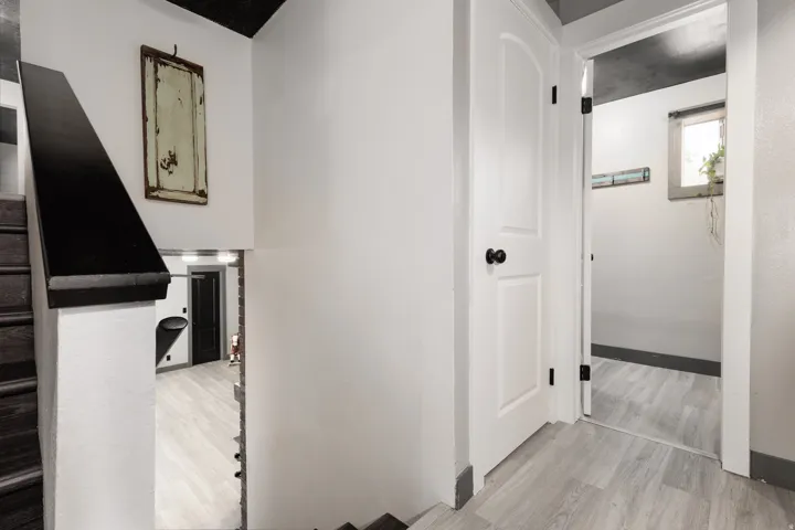 Staircase with dark wood treads and a black handrail leading to a lower level featuring light wood-finish flooring